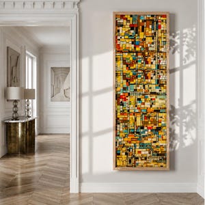 Può includere: Un'opera d'arte da parete alta e rettangolare caratterizzata da una fitta griglia di piccoli quadrati multicolori nelle tonalità del giallo, arancione, rosso, blu e nero, racchiusa in una cornice di legno chiaro, esposta verticalmente su una parete.