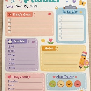 May include: A spiral-bound daily planner with a colorful design. The planner includes sections for goals, schedule, to-do list, notes, and mood tracking. The date is set to Nov. 15, 2024. Decorative elements include a sun, rainbow, and flowers.