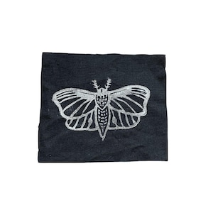 May include: A black fabric patch with a white silhouette of a moth printed on it.