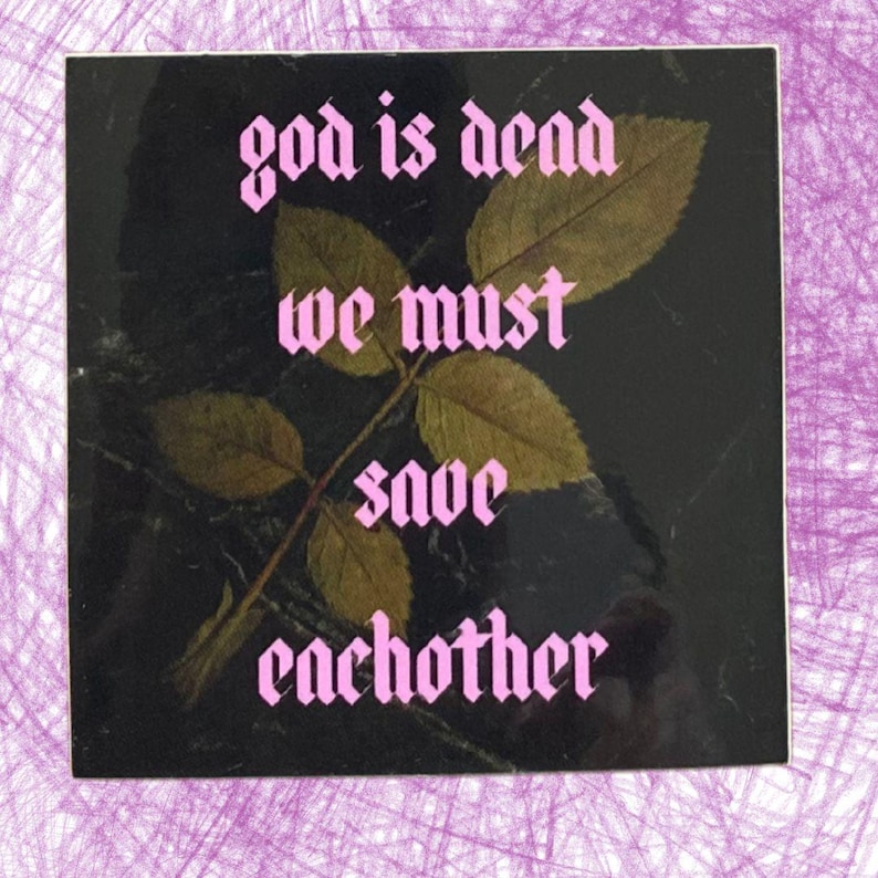 May include: Square sticker with the text "god is dead we must save eachother" in pink gothic font. The sticker has a black background with a leaf and stem design in the center.
