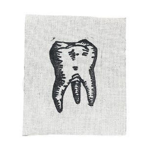 May include: A black and white illustration of a molar tooth is printed on a small, rectangular piece of off-white fabric. The tooth's roots are clearly defined, and the overall style is reminiscent of a woodcut or linocut print.