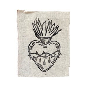May include: A black and white embroidered patch depicting a heart with a crown of thorns and flames. The heart is bleeding three drops of blood.