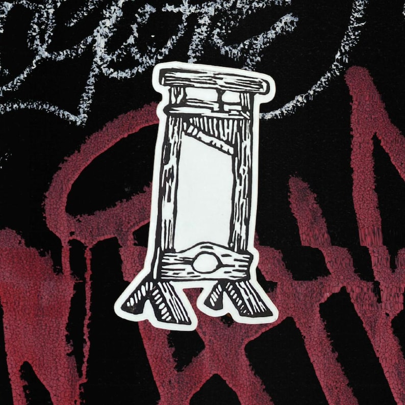 May include: A black and white sticker featuring a guillotine design. The sticker has a white border and is set against a black background with red and white graffiti-style markings.