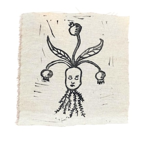 May include: Black and white linocut print on fabric depicting a stylized human face with a single eye and a crown of leaves and fruit.