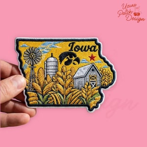 May include: Embroidered patch in the shape of Iowa, featuring a windmill, silo, barn, and corn. The word "Iowa" is in black script above a hawk and a red star. The patch has a black border and is held by a hand.