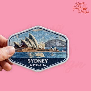 May include: Embroidered patch featuring the Sydney Opera House and Harbour Bridge against a blue sky and water backdrop. The patch is a hexagon shape with a white border and the text "SYDNEY AUSTRALIA" in white letters.