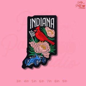 May include: Embroidered patch in the shape of Indiana, featuring the word "INDIANA" in white, a red cardinal, pink flowers, and a blue race car. The patch is approximately 3 inches to 9 inches in size.
