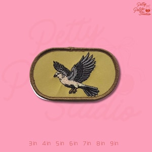 May include: Embroidered patch featuring a bird in flight, with a cream-colored body and black and gray wings. The patch is oval-shaped with a tan border and a yellow-green background. The patch measures 3 inches to 9 inches.