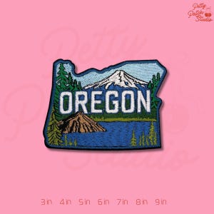 May include: Embroidered patch in the shape of Oregon, featuring a mountain, lake, and trees. The word "OREGON" is stitched in white. The patch is approximately 3 inches wide.