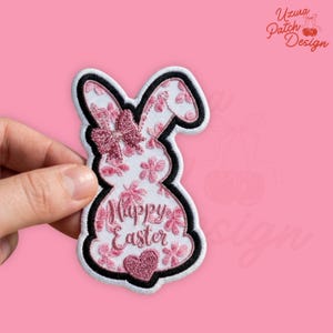 May include: Embroidered patch in the shape of a bunny with a black border. The bunny is white with pink floral accents and a pink bow. The words "Happy Easter" are embroidered on the bunny's body, with a pink heart at the bottom.