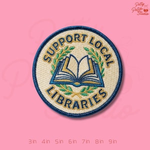 May include: Embroidered patch with the text "SUPPORT LOCAL LIBRARIES" around a central image of an open book. The patch is circular, with a blue border and a cream-colored background. The book is blue and gold, with green laurel branches.