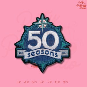 May include: Embroidered patch with a navy blue and teal design. The patch features the number "50" in white, the word "seasons", and the text "EST. 1977". The patch is in the shape of a star and baseball compass.