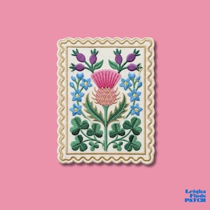 May include: Embroidered patch featuring a thistle design with pink, purple, blue, and green elements. The patch has a cream-colored background with a gold border and a scalloped edge. The patch is rectangular and has the text "Leigha Finds Patch" in the bottom right corner.