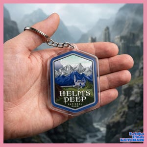 May include: A clear, shield-shaped keychain featuring a mountain landscape with the text "Helm's Deep National Park." The design includes a white castle, blue mountains, and a blue border. A silver keyring is attached.