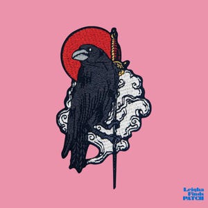 May include: Embroidered patch featuring a black raven perched on a cloud with a sword, set against a red sun. The design includes intricate details and is set on a pink background. The text "Leigha Finds Patch" is in the bottom right corner.