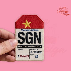 May include: A rectangular patch with a red top section featuring a gold star, and a beige bottom section. The patch reads "Vietnam Airlines SGN HO CHI MINH CITY" with flight details. The weight is listed as 18.