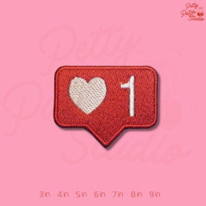 May include: Embroidered red patch in the shape of a social media like button, featuring a white heart and the number 1. The patch is on a pink background. The text "Petty Patch Studio" is in the upper right corner.
