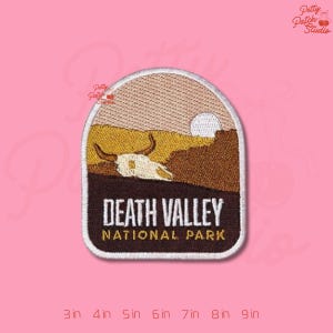 May include: Embroidered patch featuring a Death Valley National Park landscape with a desert scene, a sun, and a skull. The text "DEATH VALLEY NATIONAL PARK" is displayed in white on a brown background. The patch is in a rectangular shape with rounded corners.