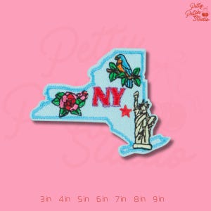 May include: Embroidered patch in the shape of New York State, featuring a parrot, roses, the letters "NY", a red star, and the Statue of Liberty. The patch is outlined in light blue and has a pink background. The patch measures 3 inches to 9 inches.