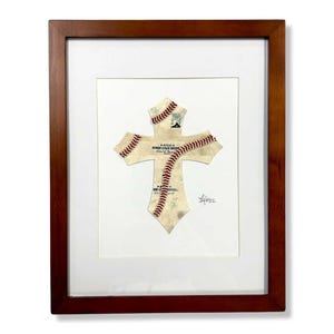 May include: A framed artwork featuring a cross made from a baseball. The cross is made from a baseball with red stitching and the text "OFFICIAL MINOR LEAGUE BASEBALL" is visible. The artwork is signed by the artist.