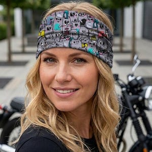 Op de afbeelding: Grijze hoofdband met een patroon van cartoonkatten met brillen, strikken en andere accessoires. De hoofdband wordt gedragen door een persoon met blond haar en een zwarte top. Op de achtergrond is een motorfiets te zien. Gemaakt van Öko-Tex stof.