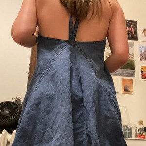 Puede incluir: Vestido halter de mezclilla en un lavado azul medio. El vestido presenta una falda acampanada y un cuello halter con cierre de lazo. Las costuras est&aacute;n acentuadas con pespuntes. Es un estilo casual de verano.