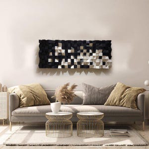 May include: A modern living room scene featuring a gray sofa with gold-legged side tables. Above the sofa hangs a large, abstract wall art piece in black, white, and gray geometric shapes. Decorative pillows and a neutral rug complete the space.