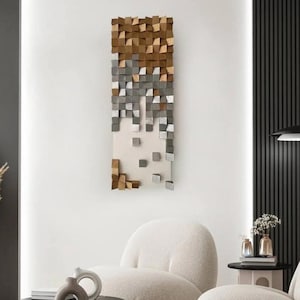 May include: A modern wall art piece with a geometric design. The artwork features a rectangular arrangement of wooden blocks in shades of brown, gray, and silver. The blocks are arranged in a cascading pattern, creating a textured and dimensional effect. The artwork is mounted on a white background.