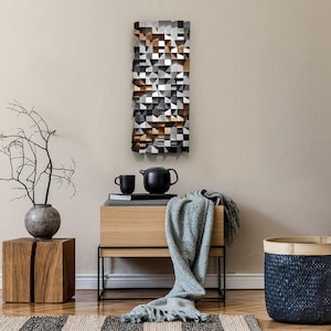 May include: A rectangular geometric wall art piece with a mosaic design in brown, grey, black, and white. The artwork hangs on a beige wall. A wooden side table with a black teapot and cup is below the artwork.