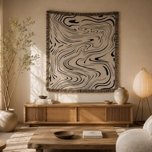 Puede incluir: Un tapiz de pared tejido cuadrado con un patrón de remolino líquido jaspeado en negro y beige con bordes deshilachados. El tejido muestra un diseño abstracto continuo de líneas fluidas, creando un efecto visual dinámico en la superficie.