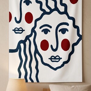K&ouml;nnte beinhalten: Wei&szlig;e Wandbeh&auml;nge mit minimalistischem Design, das zwei stilisierte Gesichter in marineblauen Umrissen zeigt. Rote Kreise dienen als Akzente. Das Kunstwerk ist an einer Holzstange mit einer nat&uuml;rlichen Kordel zum Aufh&auml;ngen befestigt.