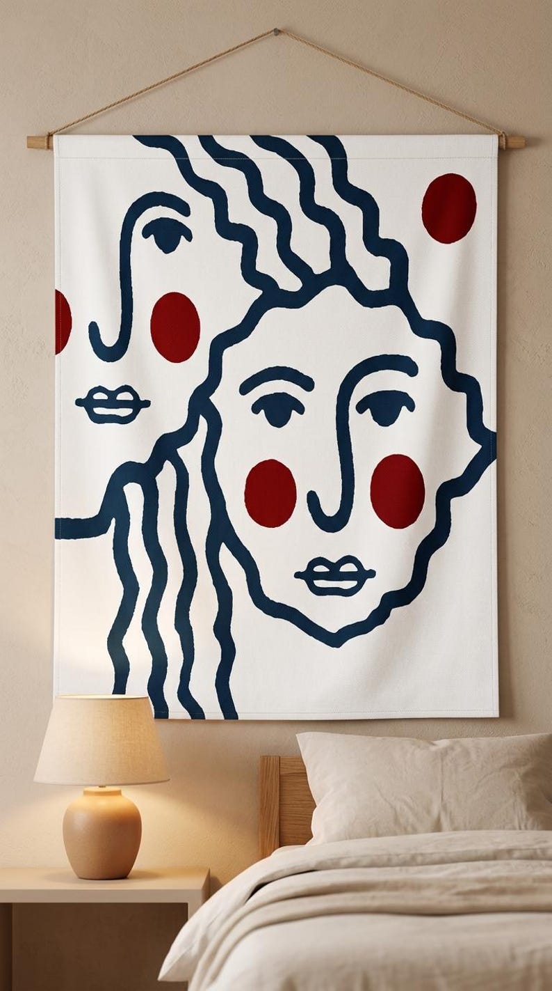 K&ouml;nnte beinhalten: Wei&szlig;e Wandbeh&auml;nge mit minimalistischem Design, das zwei stilisierte Gesichter in marineblauen Umrissen zeigt. Rote Kreise dienen als Akzente. Das Kunstwerk ist an einer Holzstange mit einer nat&uuml;rlichen Kordel zum Aufh&auml;ngen befestigt.