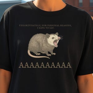 May include: Black t-shirt featuring a distressed illustration of an opossum with an open mouth. The text above reads "UNFORTUNATELY, FOR PERSONAL REASONS, I HAVE TO SAY:" and below "AAAAAAAAAAAA".