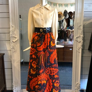 Peut inclure: Une chemise blanche à manches longues et col boutonné avec une ceinture en cuir verni noir et une longue jupe à imprimé floral orange, noir et jaune.