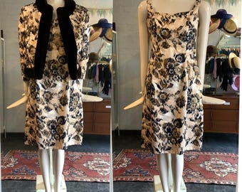 May include: A vintage dress and jacket set in a floral print with black accents. The dress has a sleeveless design and a fitted silhouette. The jacket has a fur collar and long sleeves.