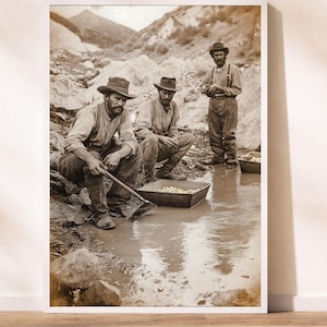 May include: Sepia-toned print of three men panning for gold. Two men are squatting near a pool of water, using tools to sift through the sediment. A third man stands nearby, observing the process. The scene is set against a backdrop of rocky terrain.