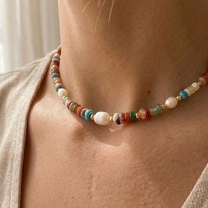 May include: A colorful beaded necklace featuring a mix of round and irregular beads in shades of red, green, blue, and white. The necklace includes a large white pearl and small gold-colored beads.