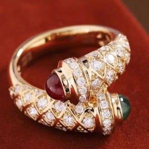 Peut inclure: Une bague ouverte en or avec un motif croisé texturé incrusté de nombreux petits diamants ronds transparents. Une extrémité de la bague est ornée d'une pierre cabochon rouge foncé lisse, tandis que l'autre extrémité présente un cabochon vert foncé.