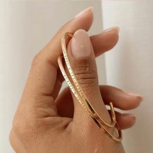 Peut inclure: Un bracelet manchette en métal doré orné de coordonnées gravées. Le bracelet fin et ouvert présente une finition lisse et polie, avec un texte numérique précis gravé sur la surface extérieure, offrant un aspect simple et épuré.