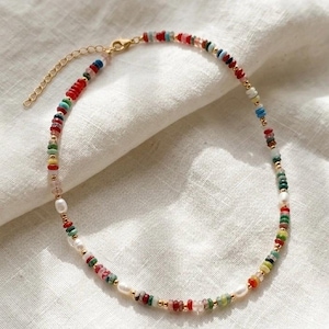 May include: A colorful beaded necklace with a gold-tone chain and clasp. The necklace features a variety of small, irregularly shaped beads in red, green, blue, and yellow, interspersed with white pearls and gold beads.