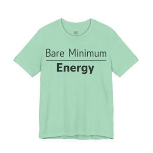 May include: A light green t-shirt with the words "Bare Minimum" above "Energy" in black, sans-serif font. The text is centered on the shirt. The shirt has short sleeves and a crew neck.