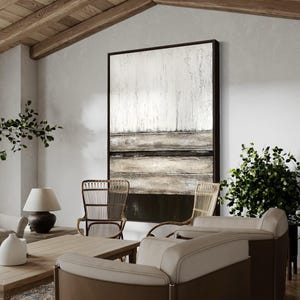 May include: A modern living room scene with a large abstract artwork in a dark frame. The room features neutral-toned furniture, including a sofa and chairs, a wooden coffee table, a lamp, and potted plants, creating a stylish and comfortable interior.