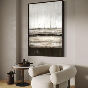 May include: Abstract artwork in a dark brown frame, with textured white, beige, and dark brown horizontal bands. A cream armchair with rounded arms and a small side table with a marble top are also visible.