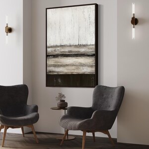 May include: A modern living room setup with two grey armchairs and a large abstract painting. The painting is framed in black and hangs above the chairs. Two wall lights with vertical tubes are mounted on the wall. A small side table is between the chairs.