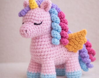 Puede incluir: Unicornio de ganchillo hecho a mano en rosa claro, con cuerno amarillo, melena multicolor y alas. El unicornio tiene los ojos cerrados y pezuñas azules. Un juguete de peluche encantador, ideal para niños o como objeto decorativo.