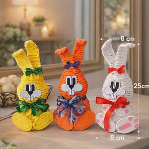 May include: Three decorative Easter bunny figurines. The bunnies are yellow, orange, and white, each with a bow. The white bunny is 25 cm tall and 8 cm wide. The yellow bunny has a green bow, the orange has a blue bow, and the white has a red bow.