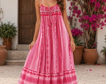 May include: A floor-length sleeveless dress in shades of light and dark pink, featuring a scoop neckline with thin straps and a tassel tie. The fabric displays a repeating geometric pattern with vertical stripes and a tiered, ruffled hemline.