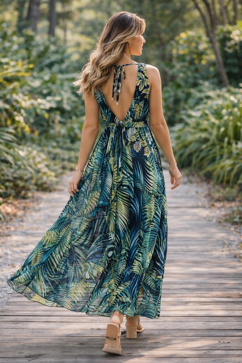 Puede incluir: Vestido largo sin mangas con estampado de hojas tropicales en tonos azules y verdes. El vestido tiene un escote en V pronunciado y un lazo en la espalda. La persona lleva tacones beige y camina por una pasarela de madera. El vestido es fluido.