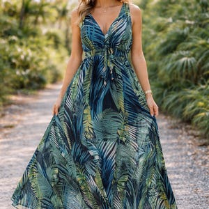 Puede incluir: Un vestido largo sin mangas con estampado de hojas tropicales en tonos azules, verdes y blancos. El vestido tiene un escote en V y un lazo en la cintura. La modelo lleva sandalias beige.