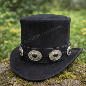 May include: A black top hat with a flat crown and a wide brim. A black band encircles the base of the crown, decorated with four circular silver-toned metal concho accents. The text IRONHIDE OUTFITTERS is printed on the side of the hat crown.